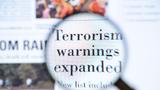 Magnifying glass showing terrorism warnings expanded text on a newspaper, photo by brightstars/Getty Images