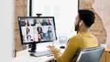A man in a yellow sweater talks to a group of people on a video conference call on his computer, photo by SDI Productions/Getty Images